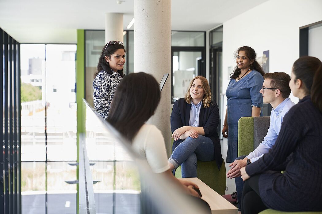 Five women and one man sit or stand together and talk to each other.